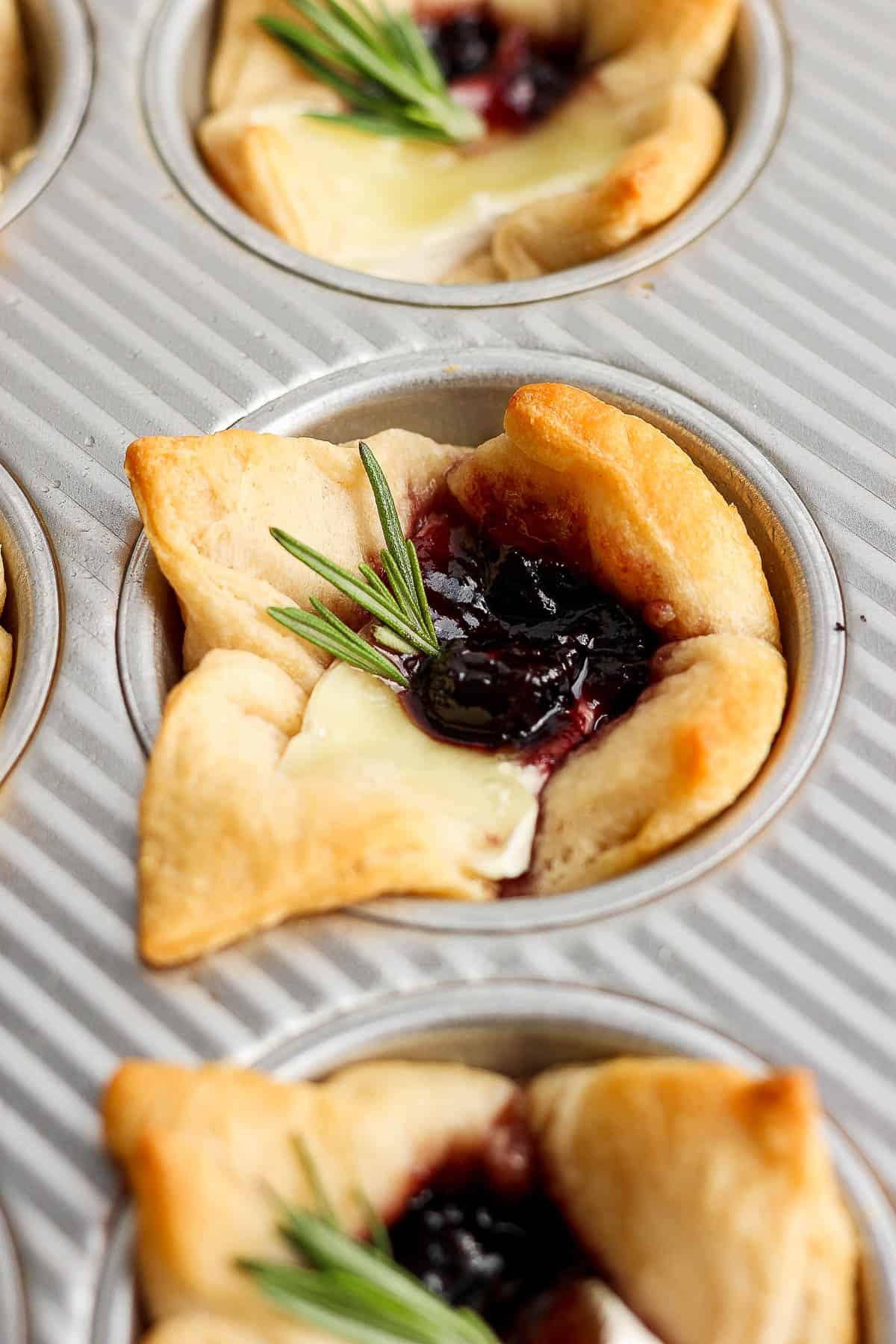 A close up of a baked brie bite with a sprig of rosemary on top.