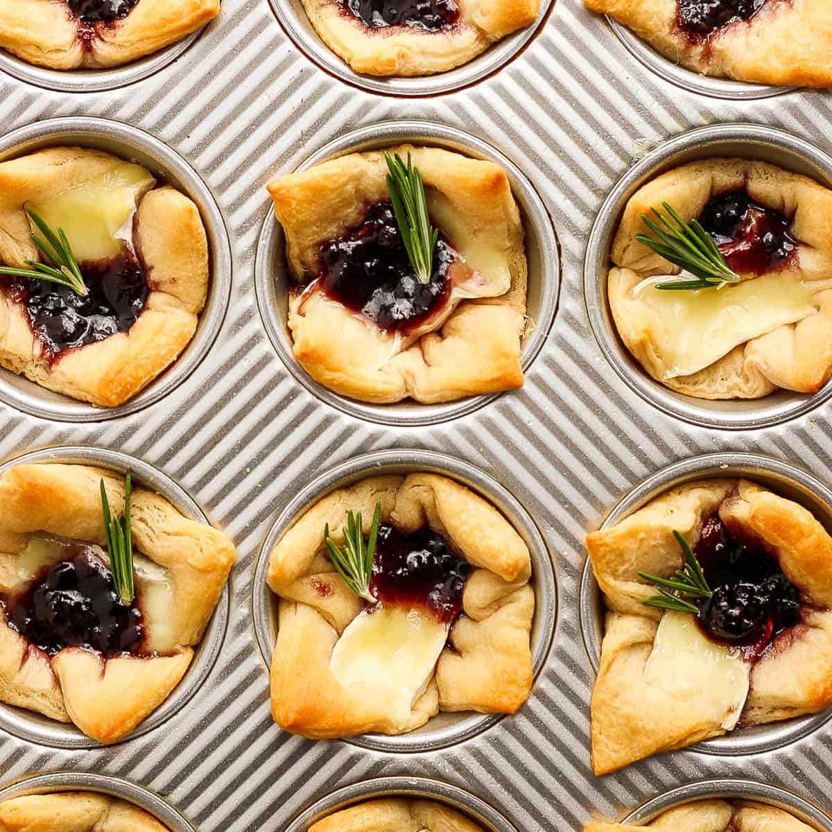 Top down shot of a muffin pan filled with baked brie bites.