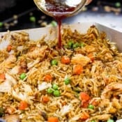 Fried rice being cooked on a Blackstone grill with someone pouring some sauce on top.