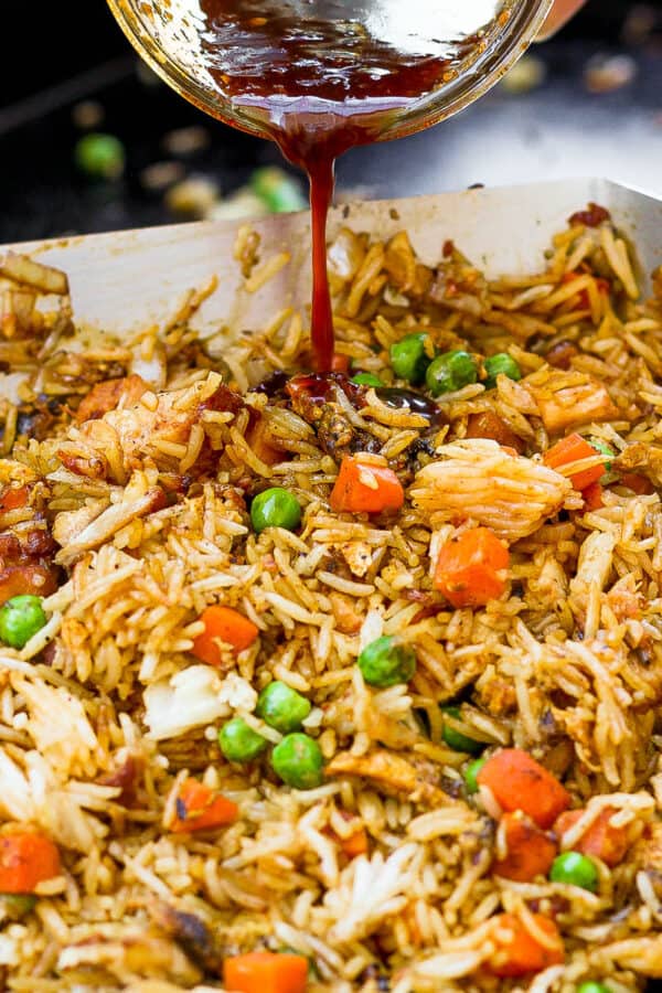 Fried rice being cooked on a Blackstone grill with someone pouring some sauce on top.