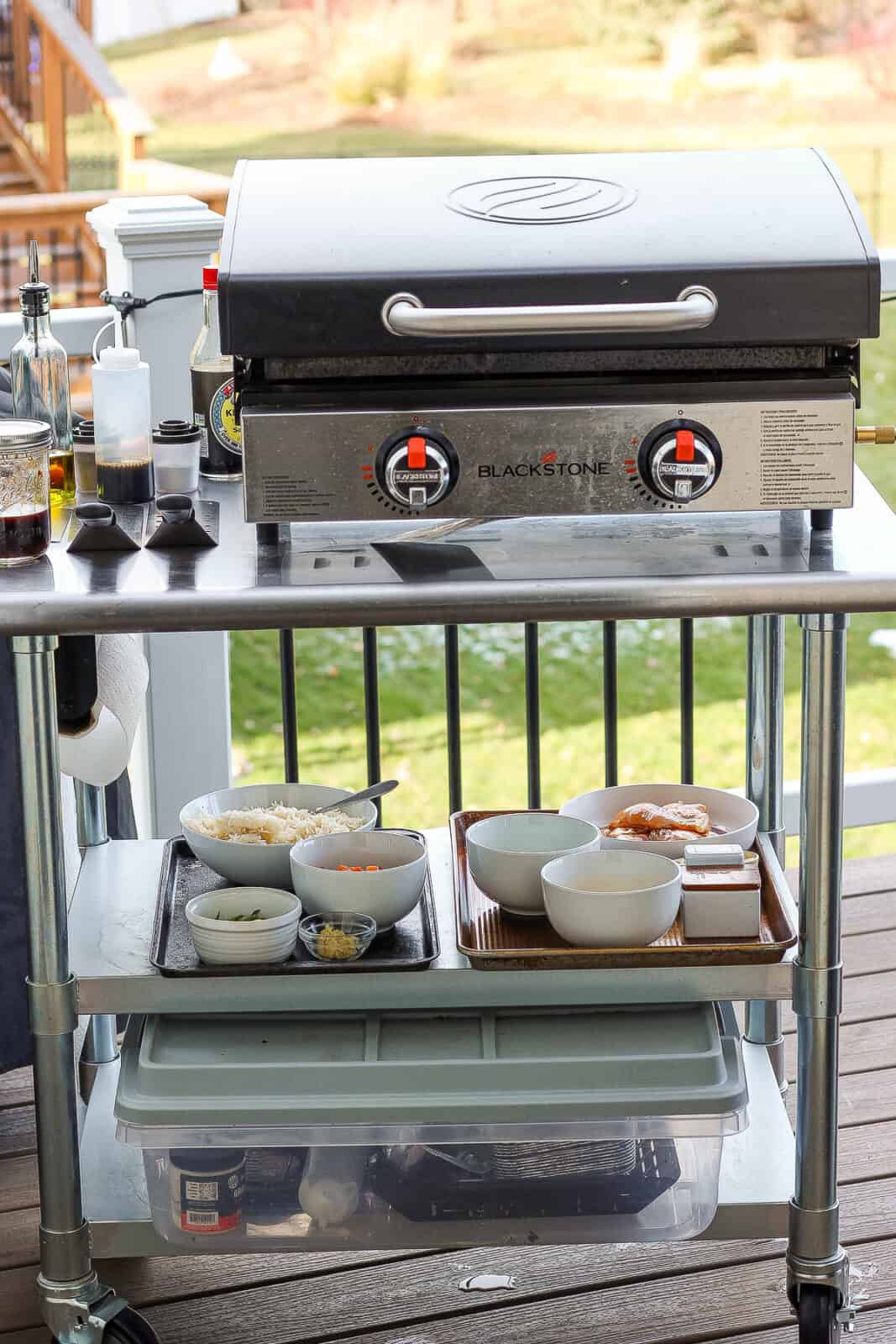 A Blackstone griddle on a metal table with bowls of ingredients for fried rice, fried rice sauce in a mason jar, and a bottle of soy sauce.