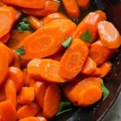 Top down shot of a pan of candied carrots garnished with chopped parsley.