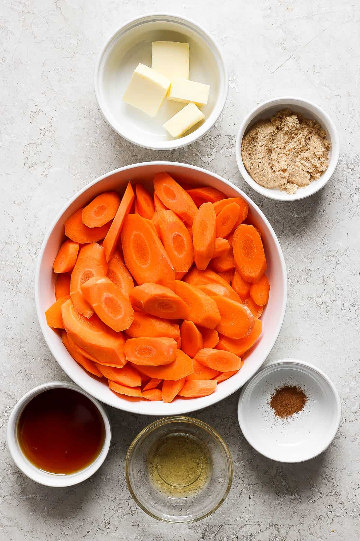 Individual bowls of chopped carrots, maple syrup, cinnamon, brown sugar, butter, and bourbon.