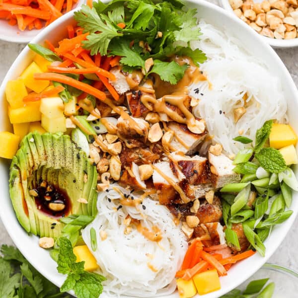 Top down shot of a chicken spring roll bowl with avocado, mango, carrots, rice noodles, chicken and peanut sauce.