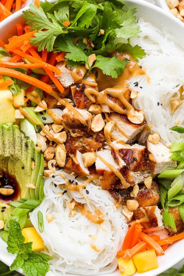 Top down shot of a chicken spring roll bowl with avocado, mango, carrots, rice noodles, chicken and peanut sauce.