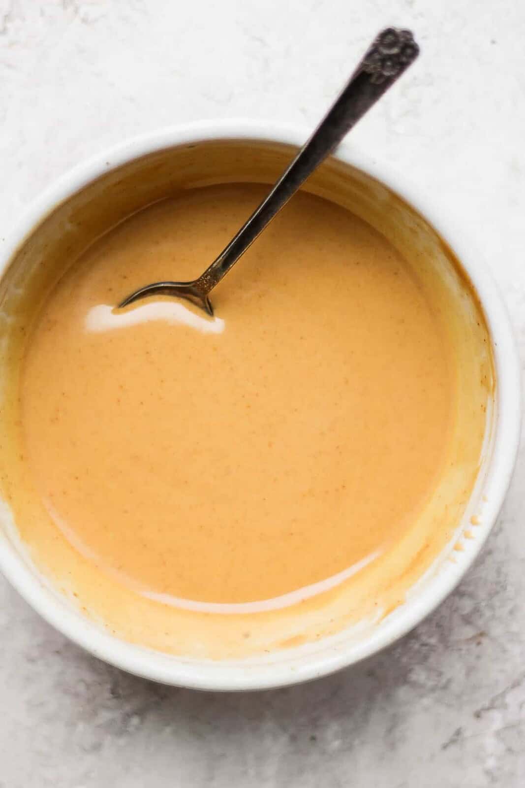 A bowl of creamy peanut sauce in a bowl with a spoon sticking out.