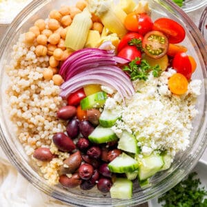 Top down shot of a bowl of couscous salad with cucumber, olives, tomatoes, chickpeas and onion.