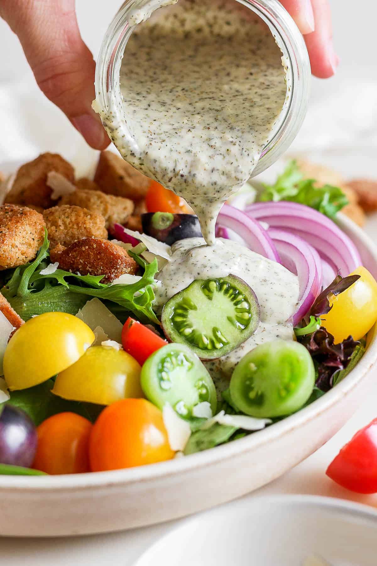 Creamy Italian dressing being poured on a house salad.