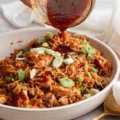 Someone pouring sauce onto a bowl of fried rice.
