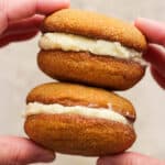 Someone holding two ginger molasses whoopie pies in their hands, stacked.