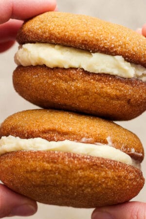 Someone holding two ginger molasses whoopie pies in their hands, stacked.