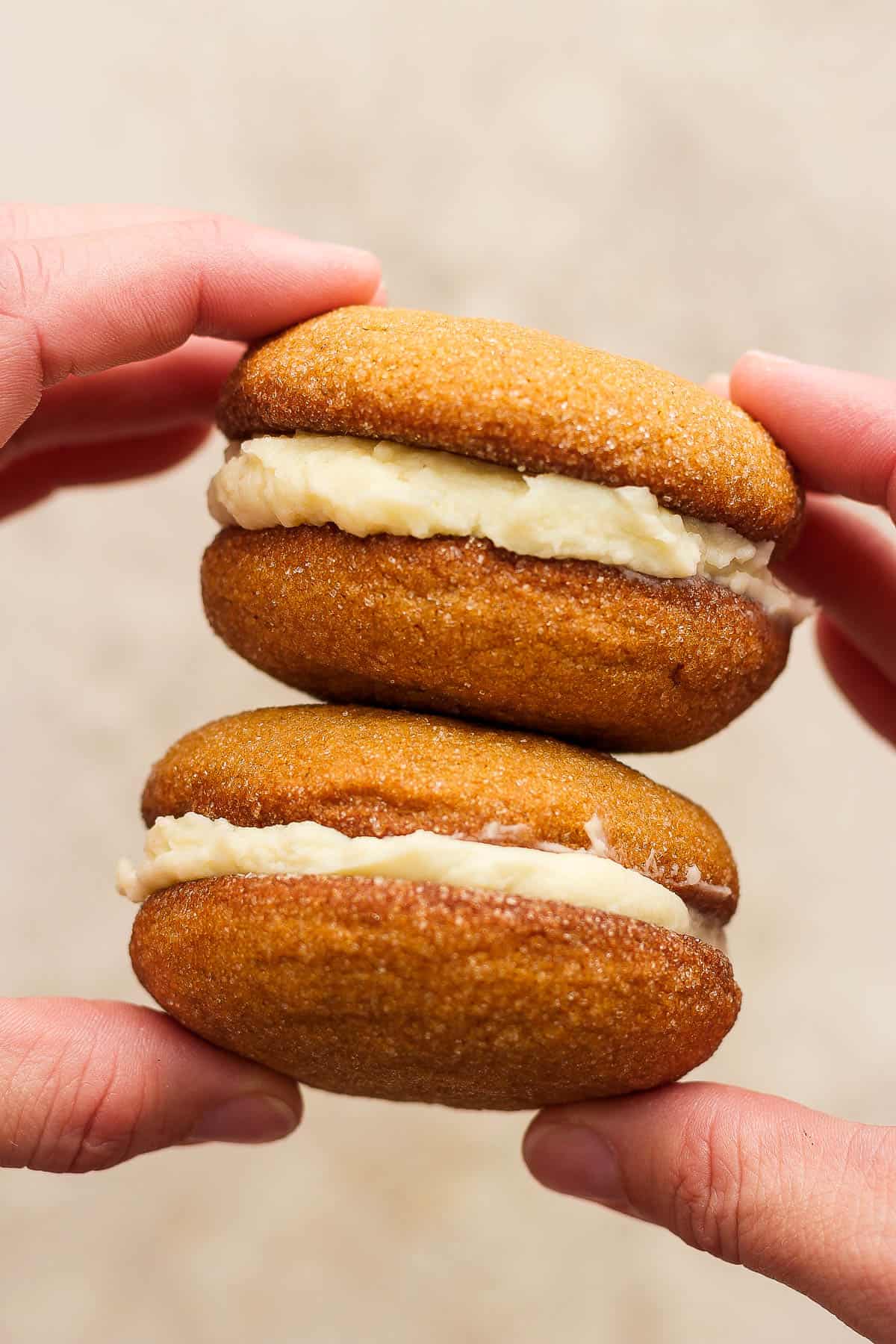 Two hands holding a stack of two ginger molasses whoopie pies.