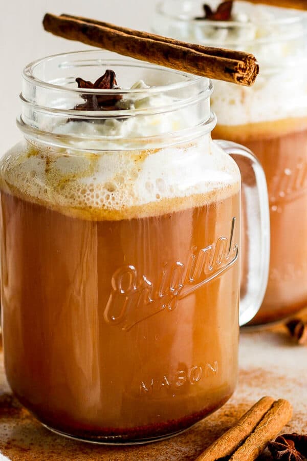 A glass mug filled with hot buttered rum and topped with whipped cream and a cinnamon stick.