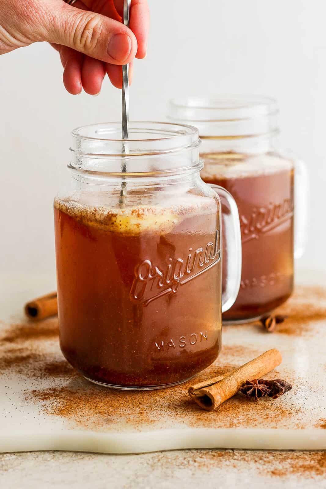 A hand using a metal stir stick to combine ingredients with water.
