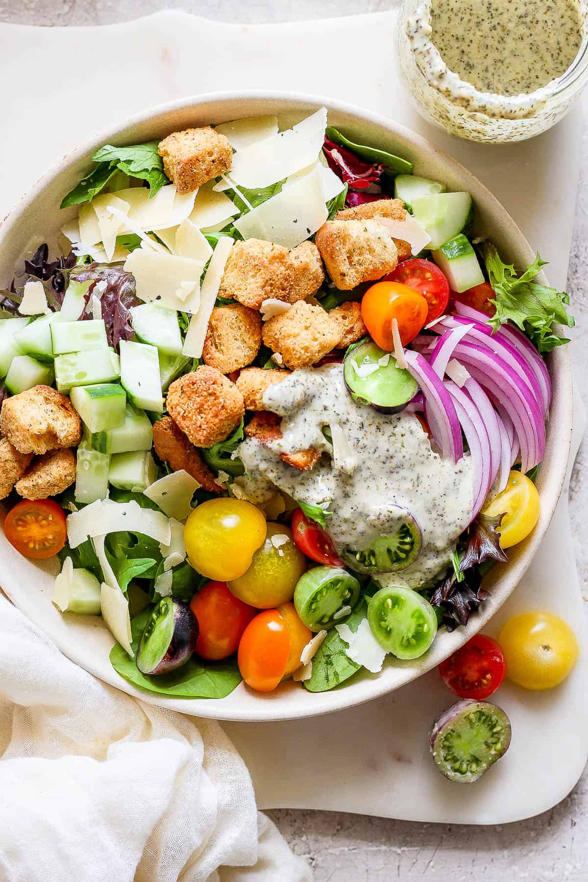 A large house salad in a white bowl with the homemade dressing on top.
