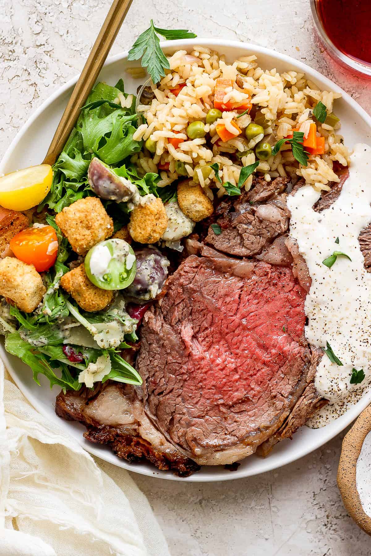 A white plate with the house salad, prime rib, and rice pilaf.