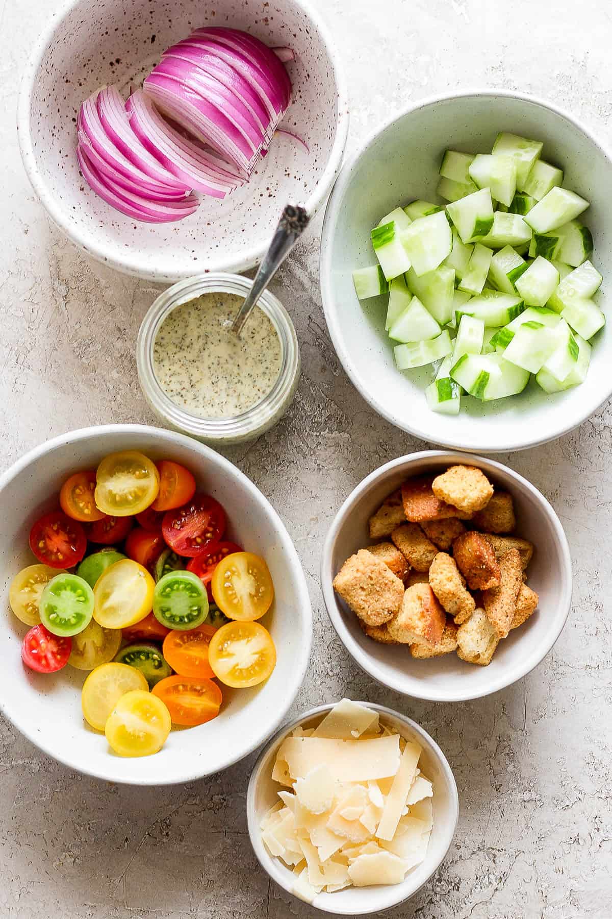 Fresh vegetables, croutons, and dressing in separate bowls.