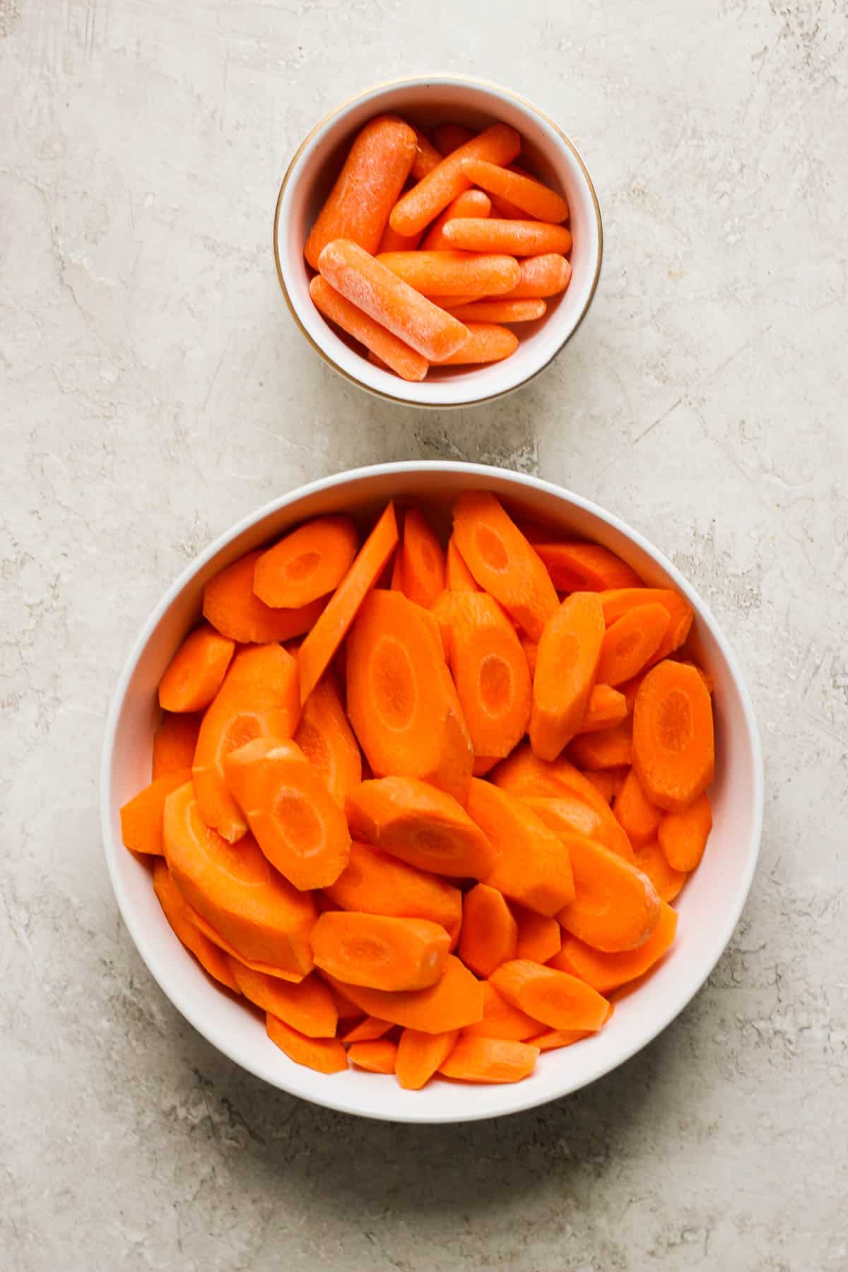 Raw baby carrots and carrot coins in white bowls.