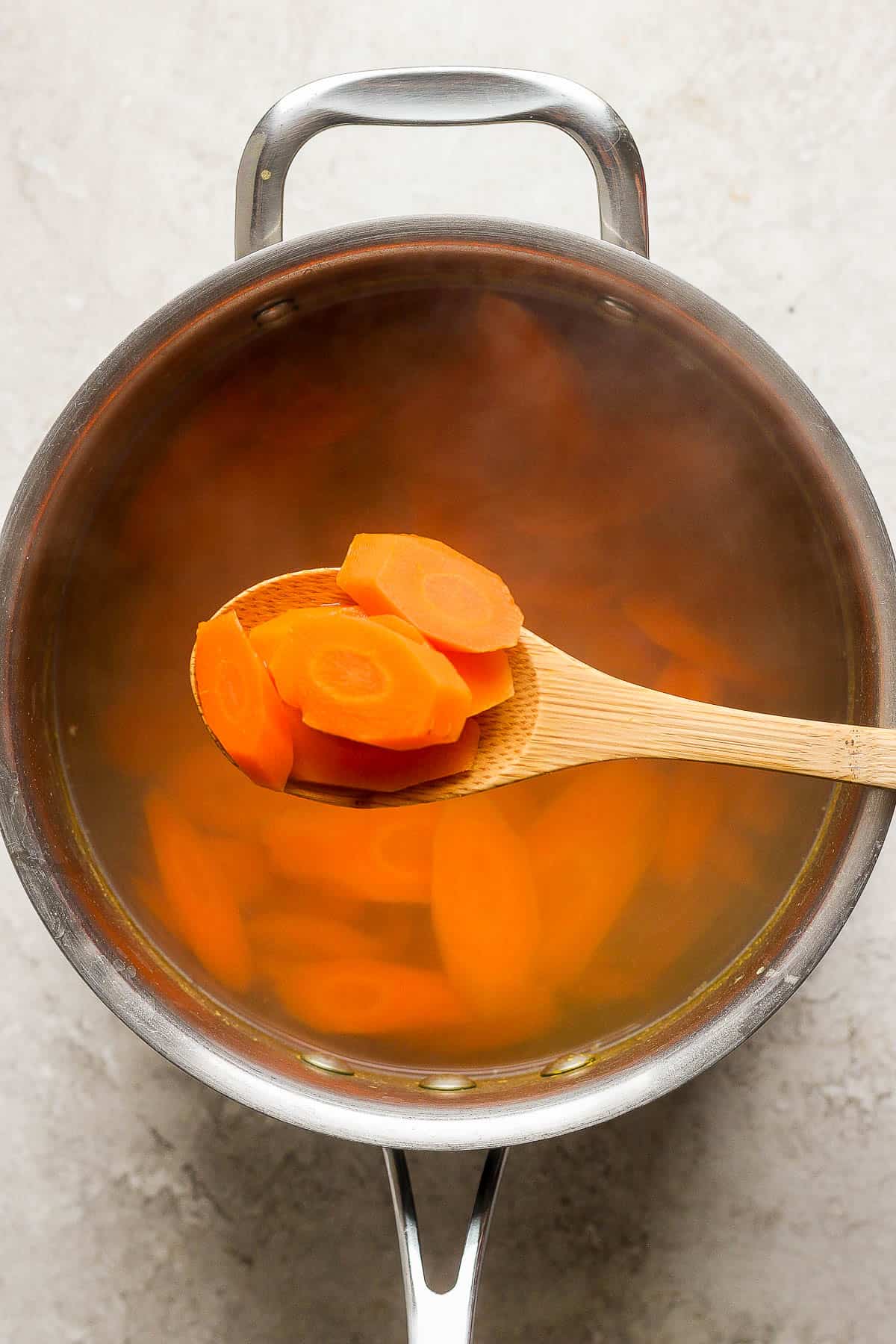 A wooden spoon scooping cooked carrots out of a pot.