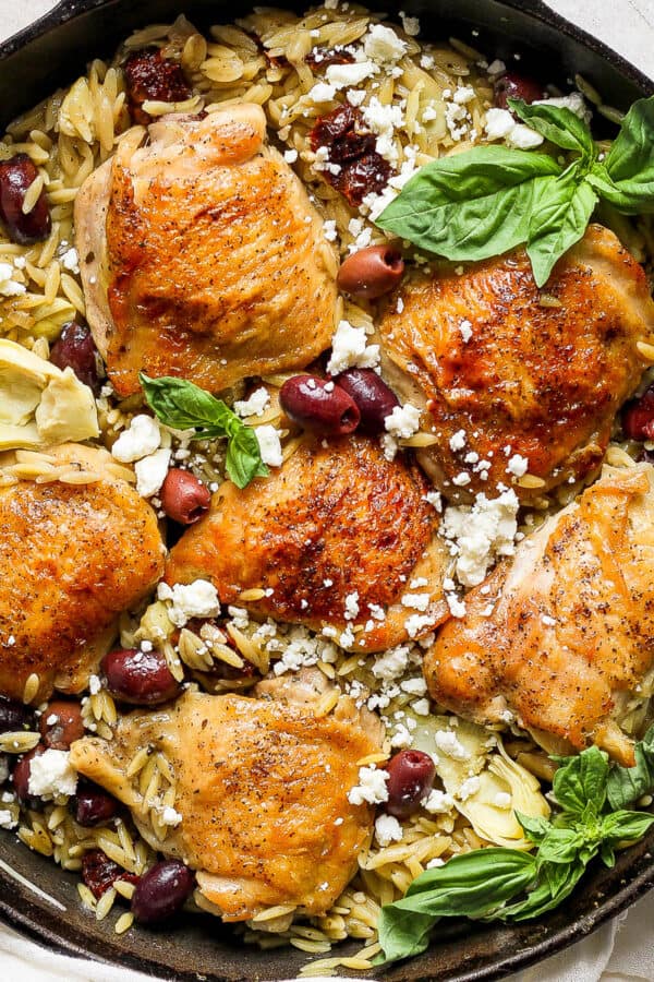 Top down shot of a kalamata lemon chicken orzo skillet with feta cheese and fresh basil on top.