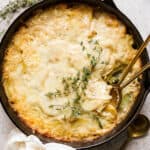 Top down shot of a cast iron skillet filled with potatoes au gratin gruyere with two spoons sticking out and fresh thyme sprigs on top.
