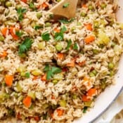 Top down shot of a braiser filled with homemade rice pilaf with a wooden spoon sticking out.