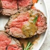 Slices of medium-rare beef tenderloin with sauce on a white plate.
