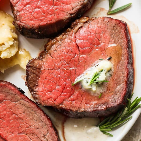 Top down shot of a plate of three slices of smoked beef tenderloin with herbed butter on top and horseradish sauce next to it.