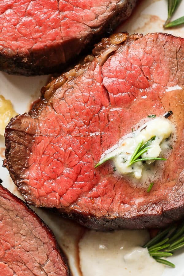 Top down shot of a plate of three slices of smoked beef tenderloin with herbed butter on top and horseradish sauce next to it.