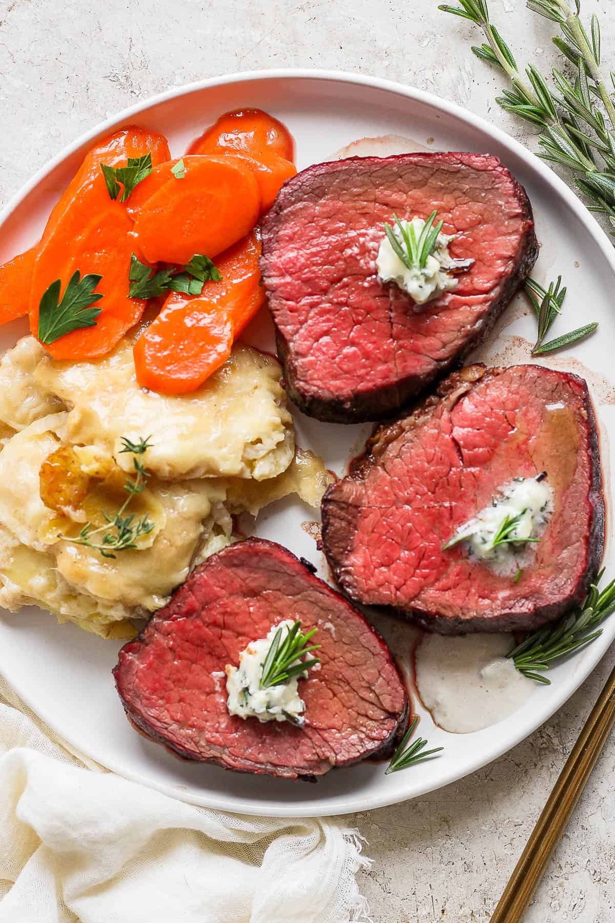 A large white plate with slices of beef tenderloin, potatoes au gratin, and candied carrots.