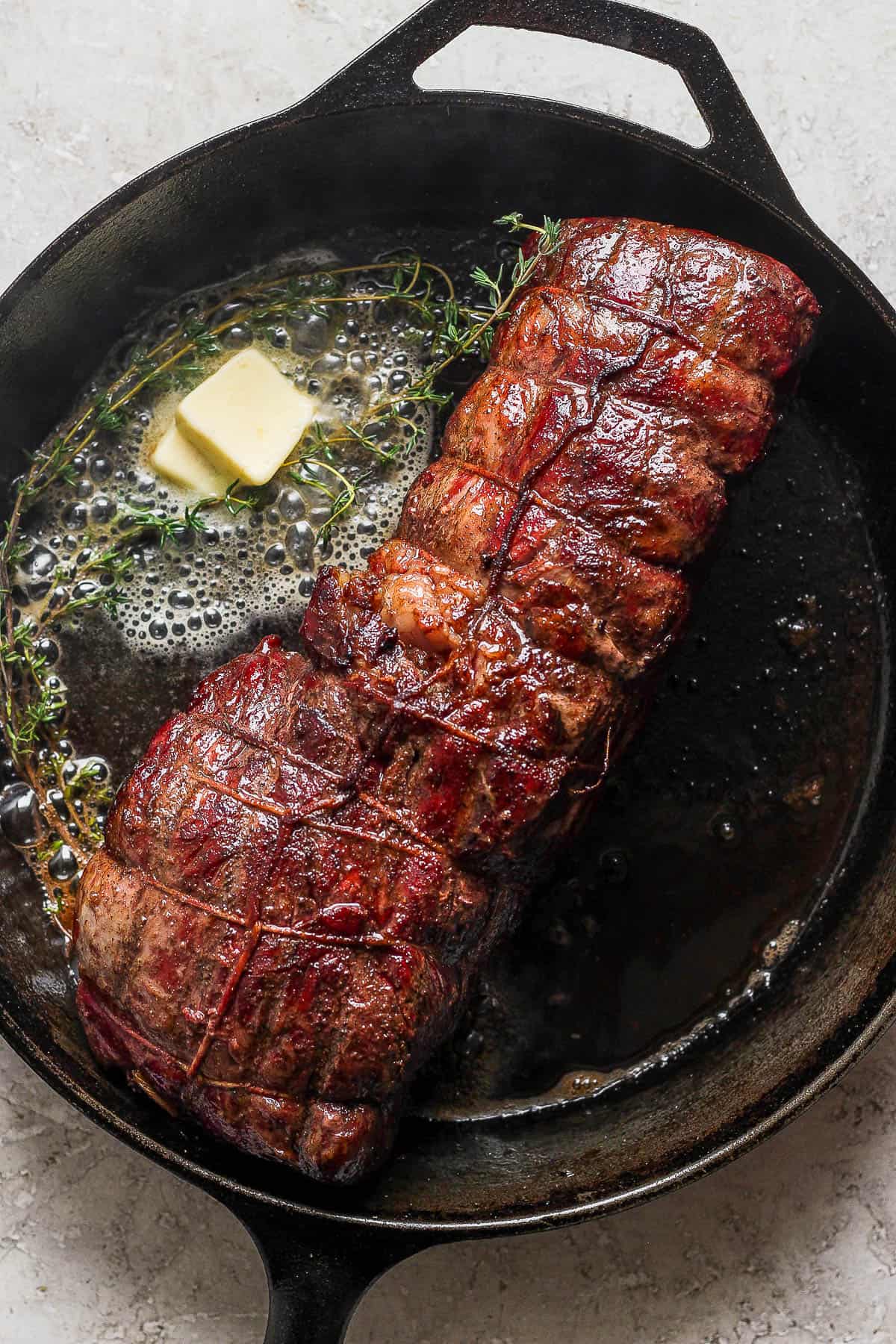 A smoked tenderloin searing in a cast iron skillet with butter and fresh thyme.