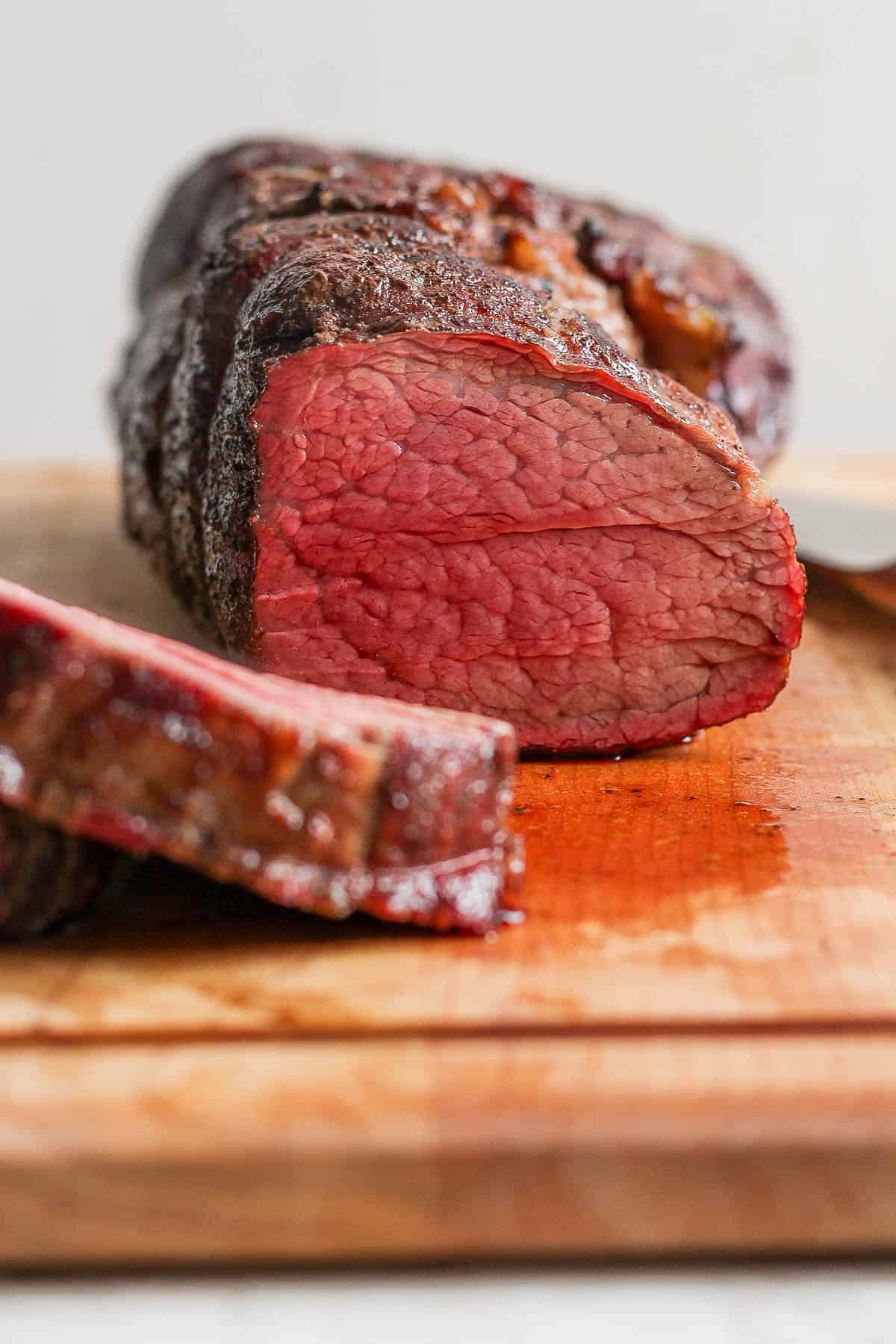 A beef tenderloin on a cutting board and being cut into slices.