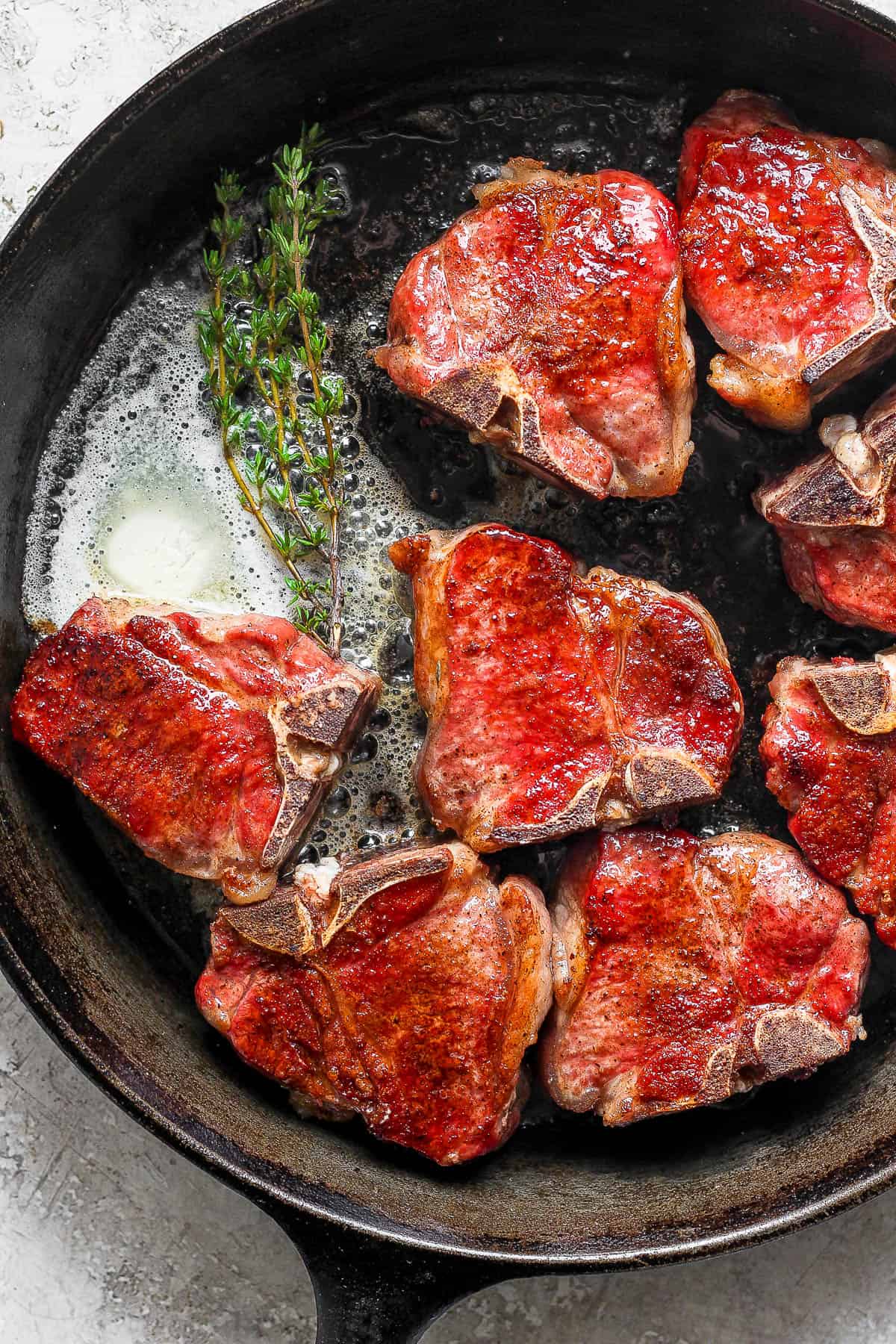 Smoked lamb chops being seared in a skillet with butter and thyme.