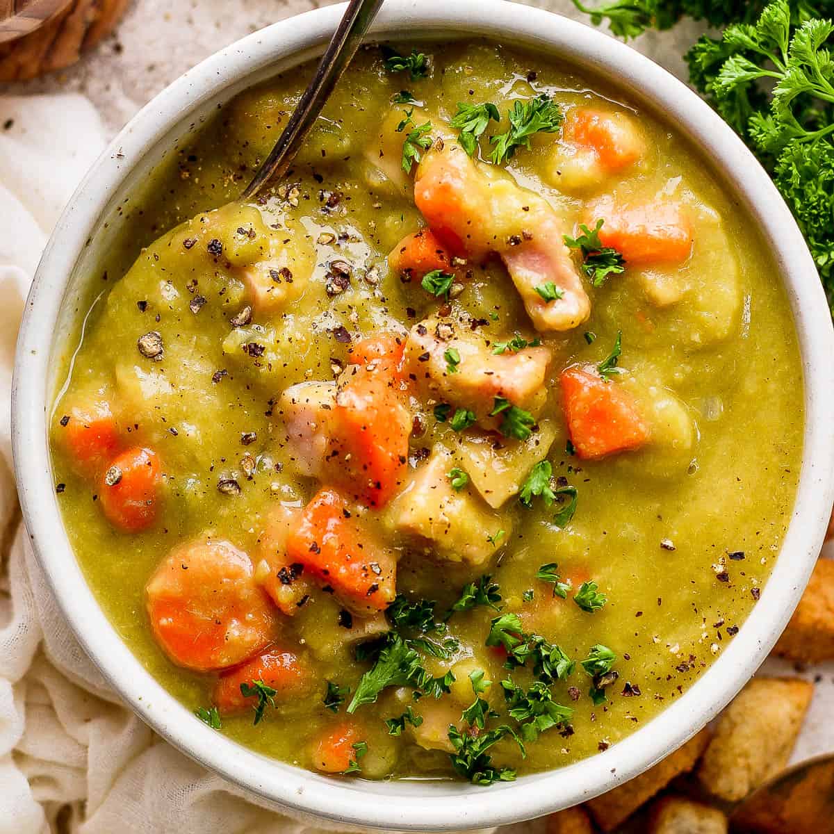 Top down shot of bowl of split pea soup with ham and a spoon sticking out.