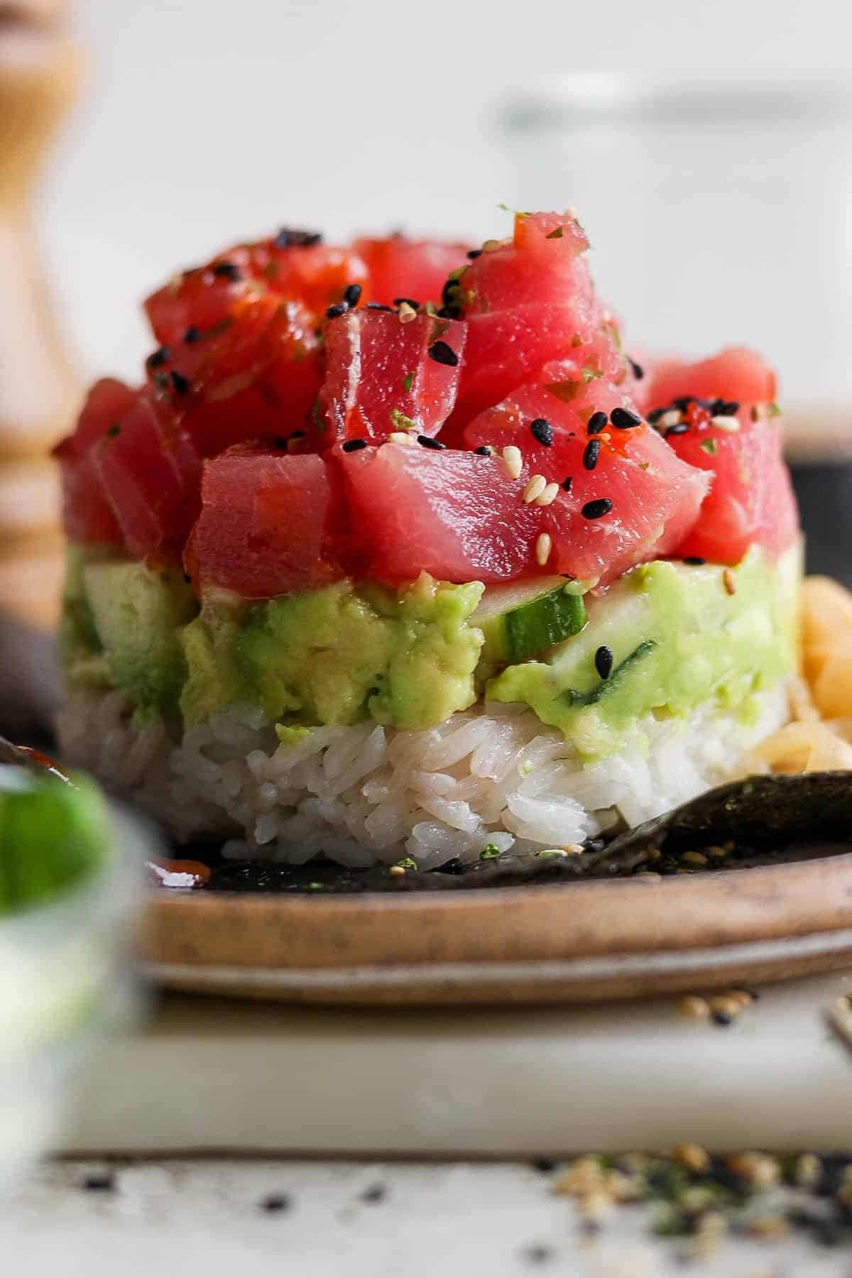 Straight on shot of a spicy tuna sushi stack with rice, avocado, cucumber and tuna layers with sesame seeds on top. 