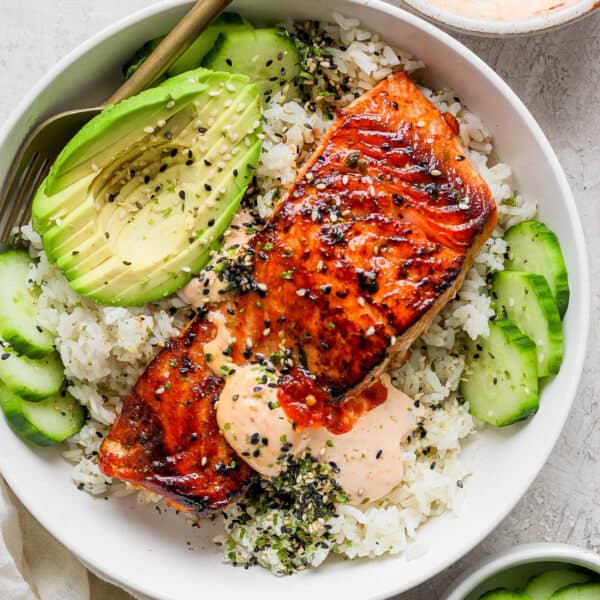 Top down shot of a piece of baked salmon on rice with avocado, cucumber and spicy mayo.