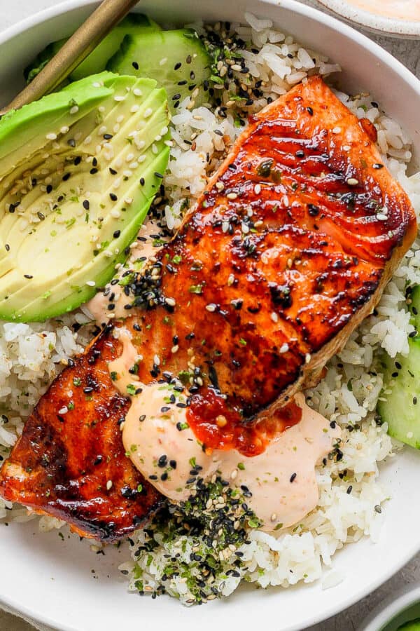 Top down shot of a piece of baked salmon on rice with avocado, cucumber and spicy mayo.