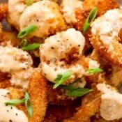 A pile of bang bang shrimp coated in sauce with sliced green onions on top.
