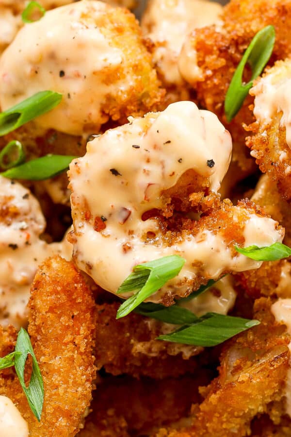 A pile of bang bang shrimp coated in sauce with sliced green onions on top.