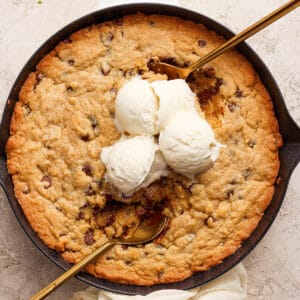 Top down shot of a cookie skillet with three scoops of vanilla ice cream and two gold spoons sticking out.