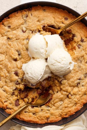 Top down shot of a cookie skillet with three scoops of vanilla ice cream and two gold spoons sticking out.