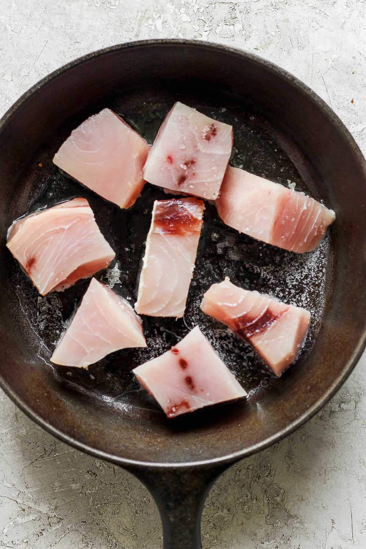 Large pieces of swordfish searing in a cast iron skillet.