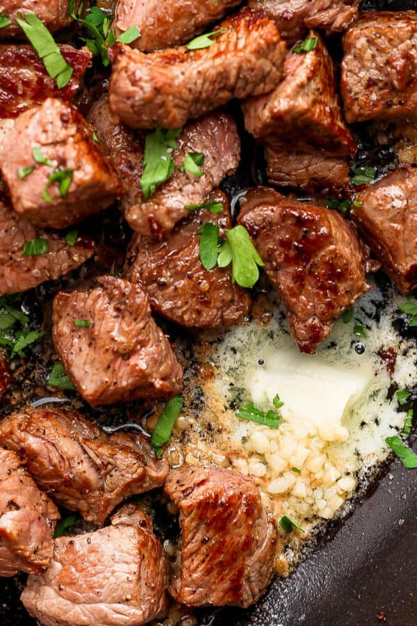 Top down shot of a cast iron skillet filled with garlic butter steak bites with fresh parsley as garnish.