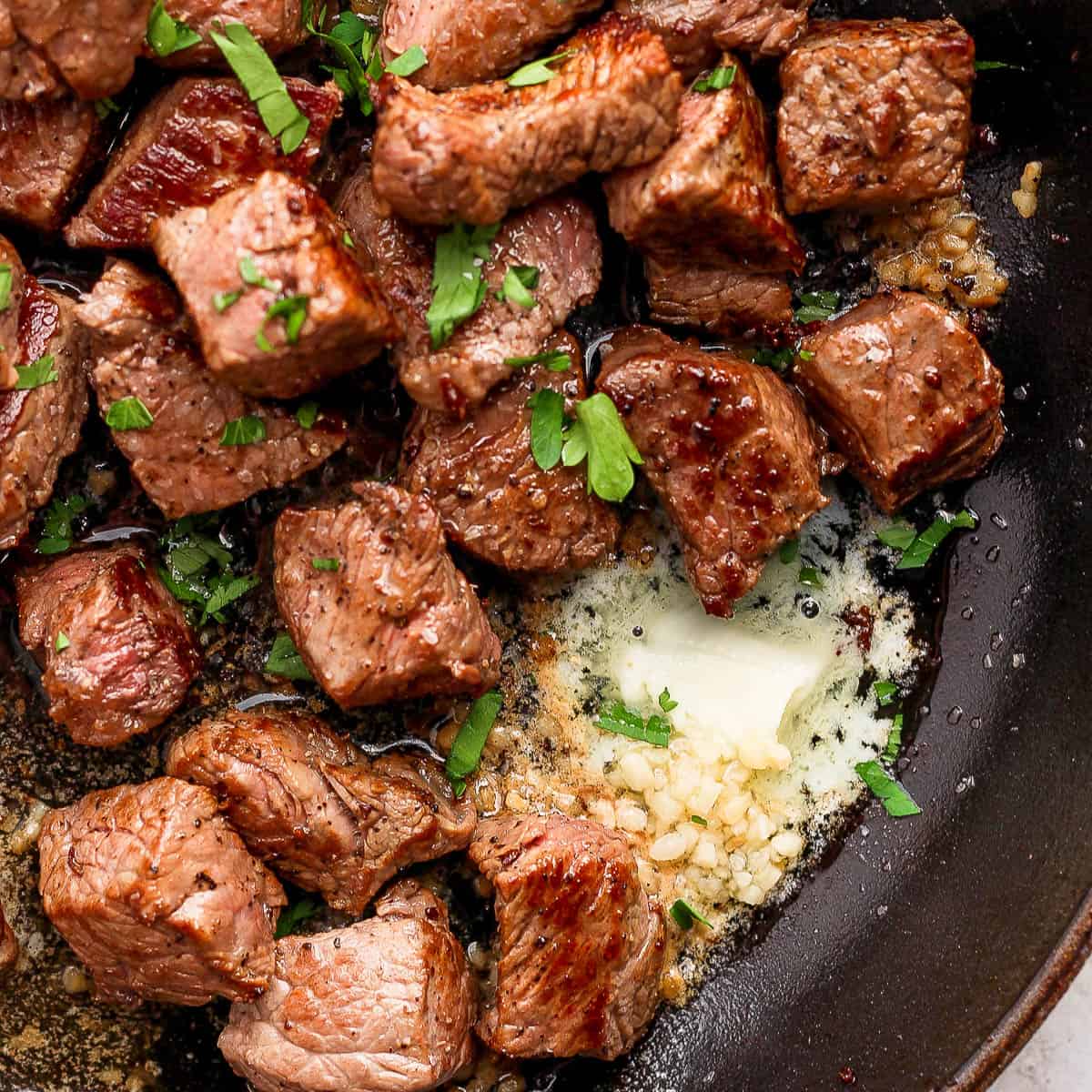 Top down shot of a cast iron skillet filled with garlic butter steak bites with fresh parsley as garnish.