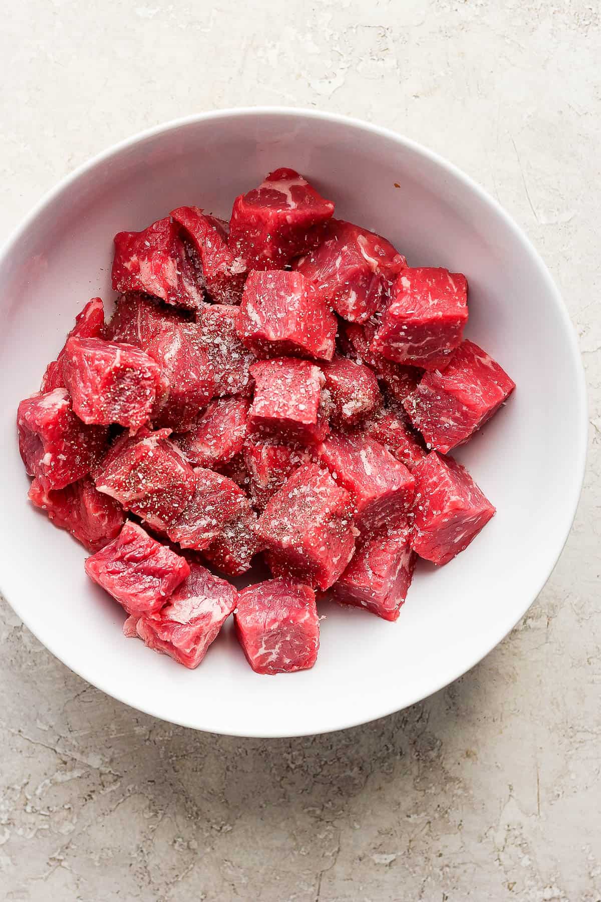 Raw steak bites in a white bowl with salt and pepper.
