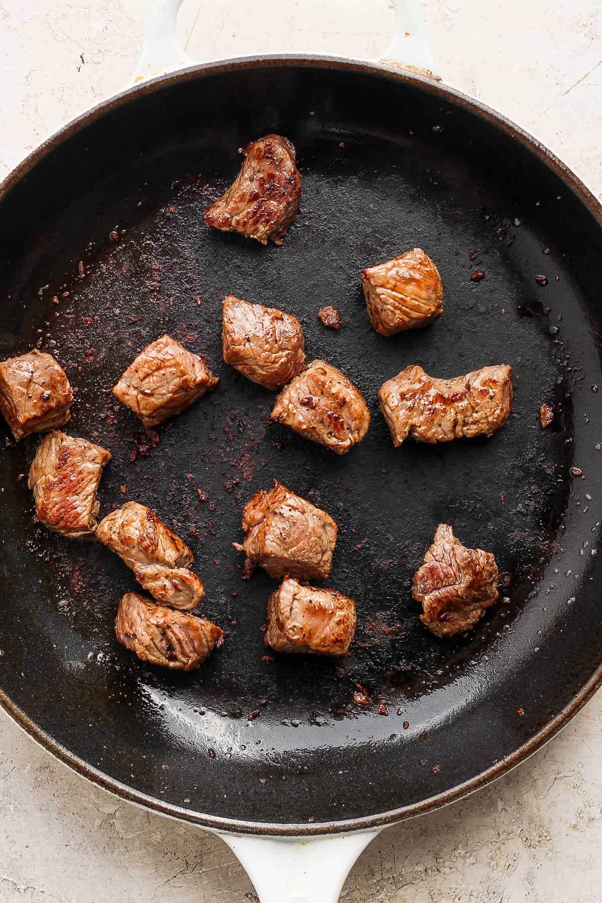Some steak bites searing in a cast iron skillet.