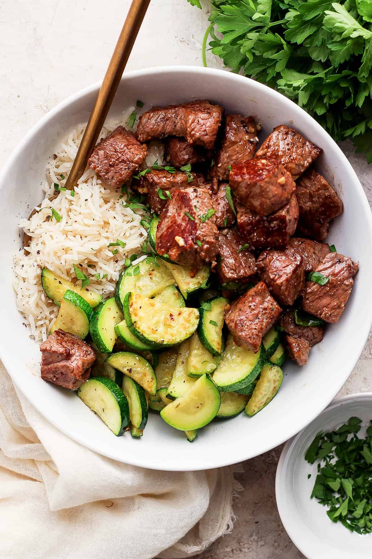 Garlic butter steak bites in a white bowl with white rice and zucchini.