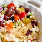 Side angle shot of a Greek layer dip in a dish with some of the bottom hummus layer exposed.