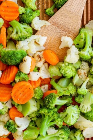 Top down shot of a pan of roasted frozen vegetables with a wooden spatula sticking out.