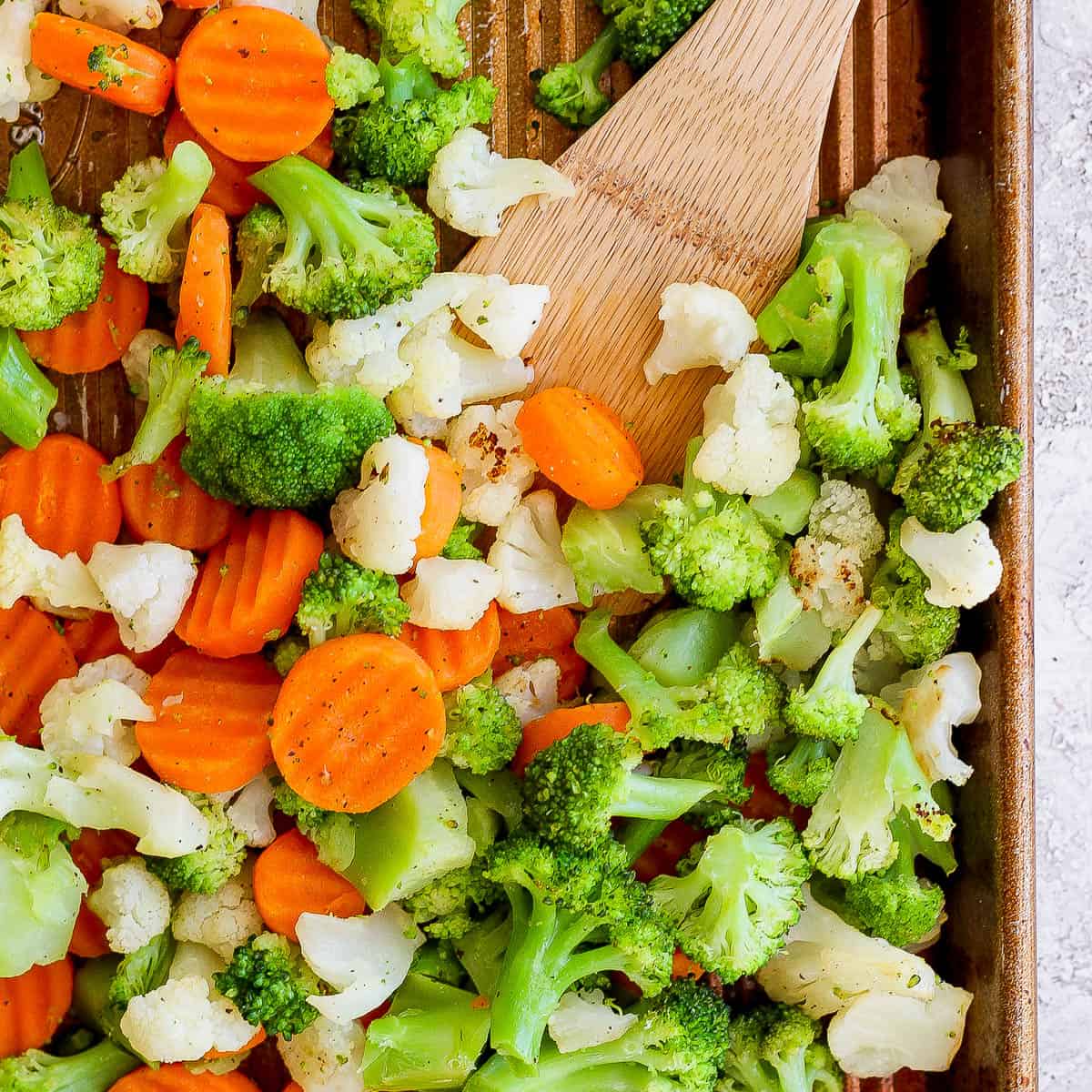 Top down shot of a pan of roasted frozen vegetables with a wooden spatula sticking out.